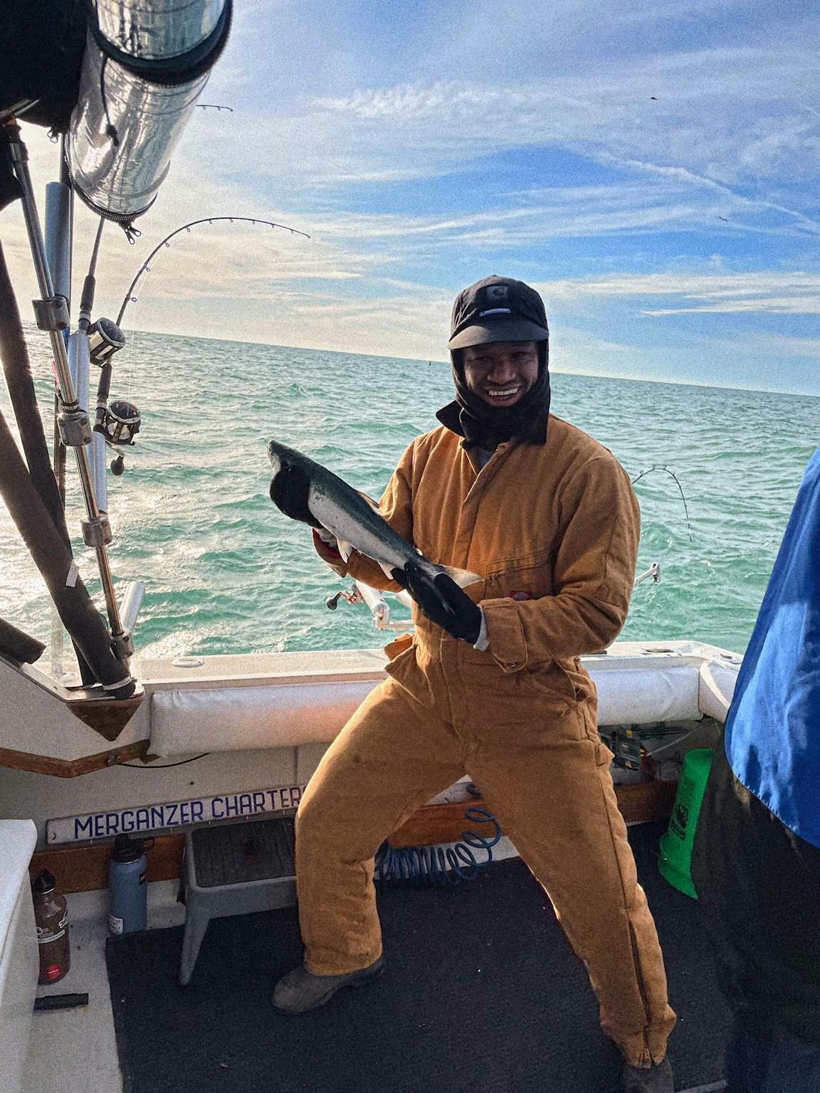 A person wearing a yellow boilersuit holds a medium-sized fish.